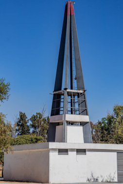 Çatısı açık mavi gökyüzüne karşı üçgen şeklinde çelik olan küçük bir bina, arka planda yeşil ağaçlar Avila Camacho halk parkında güneşli bir gün, Guadalajara, Jalisco