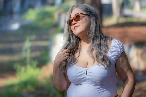 一位拉丁美洲老年旅游妇女的蜡像 背景模糊 容貌迷人 喜欢在公园散步 头转过来 长长的白发 太阳镜 — 图库照片