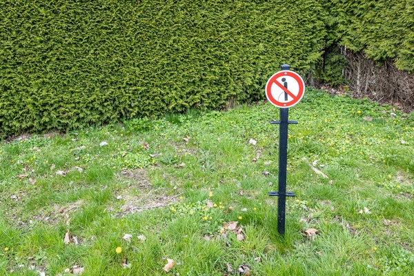 Public park with sign: No pee, it is forbidden to urinate in this place or on grass, against green vegetation, round symbol of red, white and black colors with a drawing of a man urinating