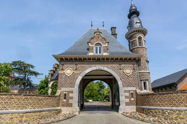 Mavi gökyüzüne karşı Borgharen Kalesi 'ne kemerli giriş, küçük pencereli kubbe, dairesel kule, tuğla duvarlar ve çitler, arka planda ağaçlar, Güney Limburg, Hollanda' da güneşli bir bahar günü.