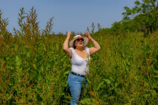 Stock image Latin American woman in a hat and sunglasses among wild plants in the Dutch countryside, white blouse and jeans, sunny spring day in Maasvallei nature reserve, South Limburg in the Netherlands