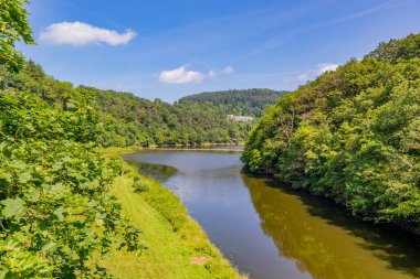 Stausee Bitburg rezervuarındaki Prum nehri su yüzeyine yansıyor, arka planda bol yeşil yapraklı ağaçlar ve dağlar, Almanya 'da güneşli bir bahar günü