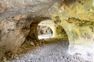 Boş bir mağaranın içindeki tüneller, düzensiz doku ve çatlaklarla dolu duvarlar, arka planda kumlu zemin üzerindeki taşlar, Belçika 'nın Vise kentindeki Sint-Pietersberg bölgesinde bulunan Thier de Lanaye doğa rezervi.