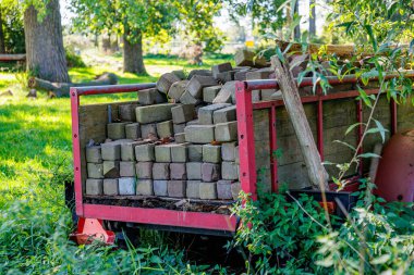 Tuğlaları ve iki kütüğü olan taşralı bir karavan çiftliğin arka bahçesindeki terk edilmiş yeşil bitki örtüsü, ağaçlar ve güneş ışığı bulanık arka planda, güneşli yaz günü