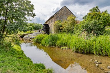 Arka planda yaşlı Eper veya Wingbergermolen su değirmeni, bulutlarla kaplı gökyüzüne karşı yapraklı ağaçlar Terpoor, Epen, South Limburg, Hollanda 'da bulutlu bir gün