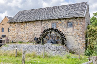 Geul nehrindeki eski taş bina, Eper ya da Wingbergermolen su değirmeni, arka planda iki pencere, ağaç ve yabani bitki örtüsü, Terpoor, Epen, Güney Limburg, Hollanda 'da bulutlu bir gün