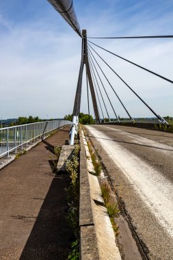 Lanaye kablo destekli köprü, taşıt yolu ve yaya ya da bisiklet yolu, kule, pilon, büyük parke ve kablolar, arka planda sisli mavi gökyüzü, asfaltta yabani bitkiler, Vise, Belçika 'da güneşli bir gün.