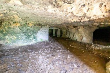 Boş bir mağaranın içi, düzensiz dokusu ve çatlakları olan duvarlar, arka planda beton destekler veya sütunlar, Belçika 'nın Vise kentindeki Sint-Pietersberg bölgesinde bulunan Thier de Lanaye doğa rezervi.