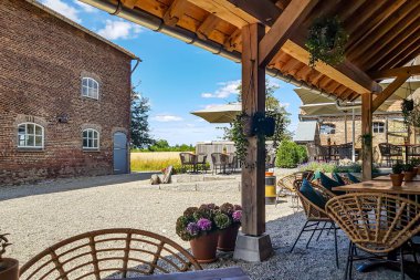 Ahşap masa ve sandalyeli bir kırsal restoranın terası, pencereli tuğla duvar ve arka planda bulanık mavi gökyüzü, güneş şemsiyeleri, güneşli bir günde dinlenmek ve dinlenmek için yer