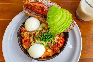 Chorizo ve graten ile patates, haşlanmış yumurta, domates sosu, soğan ve yanında domuz pastırmalı kızarmış ekmek ve beyaz tabakta avokado. Besleyici kahvaltı konsepti