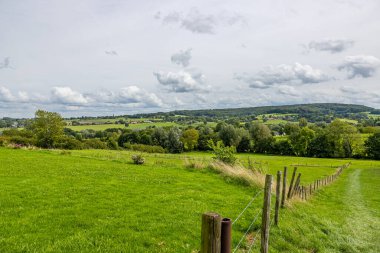 Hollanda 'nın panoramik manzarası, ahşap direkler ve tel örgüler entrikalar, ağaçlar, tepeler, arka planda bulutlarla kaplı gökyüzüne karşı köyler, Epen, Güney Limburg, Hollanda' da güneşli bir gün