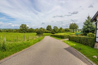 Tarlalar ve tarlalar, yeşil çimenler ve yapraklı ağaçlar, mavi gökyüzü beyaz bulutlarla kaplı, Epen, Güney Limburg, Hollanda 'da güneşli bir gün