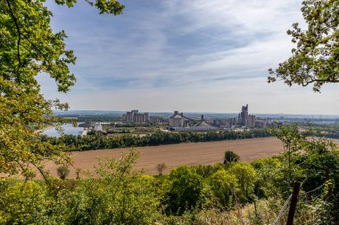 Ağaçların yeşil yaprakları, çimento fabrikası, çimento fabrikası, Albert kanalı ve ufuktaki sisli mavi gökyüzü, Belçika 'nın Vise kentinde güneşli bir yaz günü sonrasında panoramik bir tarla çerçevesi oluşturur.