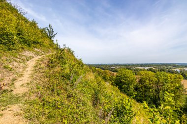 Dağ yamacında yürüyüş, yemyeşil bitki örtüsü ve ağaçlar, arka planda Maas nehri ve ufuk, Belçika 'nın Sint-Pietersberg bölgesinde Thier de Lanaye doğa rezervi, Belçika' nın Vise şehrinde güneşli bir gün.