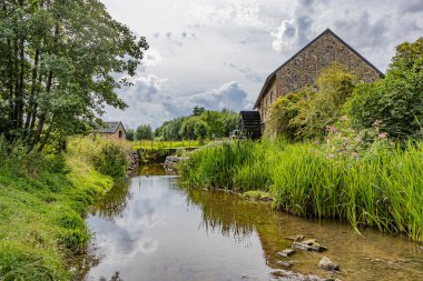 Arka planda Eper su değirmeni veya Wingbergermolen ile River Geul, bulutlarla kaplı gökyüzüne karşı yabani bitki örtüsü ve ağaçlarla çevrili, Terpoorterweg, Epen, South Limburg, Hollanda 'da bulutlu bir gün