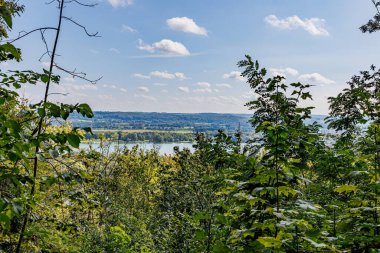 Caestert Platosu 'ndaki yemyeşil ağaçların, Maas Nehri' nin ve arka plandaki Hollanda kırsallarının, Hollanda ile Belçika arasındaki güneşli bir yaz gününün, Riemst, Belçika 'da sisli bir mavi gökyüzünün manzarasına bakın.