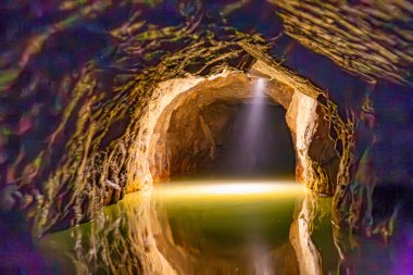 Remouchamps mağaralarında bir yeraltı nehrinin içi bir lamba ışığıyla aydınlatılmış, düzensiz ve pürüzlü duvarları olan bir tünel, su yüzeyinde yansıma, önünde bulanık bir etki, Aywaille, Belçika