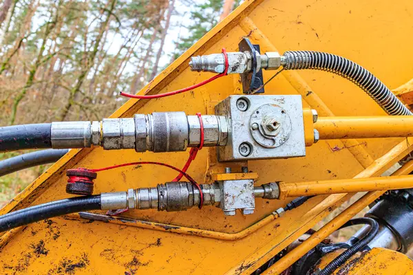 Components of a hydraulic arm of a grab excavator, connectors, hoses, cables, couplings, cylinder and different attachment, bare trees in blurred background