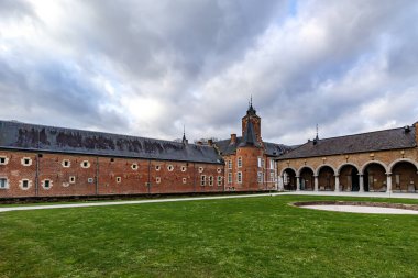 Yeşil çimenli açık alan, arka planda 16. yüzyıl Alden Biesen şatosu binaları, pencereler, tuğla duvarlar, gable çatı ve dairesel kuleler, Bilzen, Limburg, Belçika 'da bulutlu bir gün