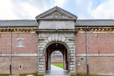 16. yüzyıl Alden Biesen Kalesi 'nin kemerli girişi, tuğla duvarlar ve gable çatısı, arka planda yeşil çimenler olan avlu, Bilzen, Limburg, Belçika' da bulutlu bir gün.