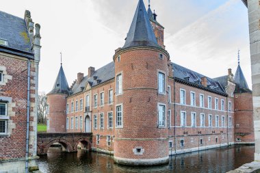 Arka planda köprü, köşe kuleleri, tuğla duvarlar ve gable çatısı olan Alden Biesen Kalesi 'ni çevreleyen hendek, 16. yüzyıl binası, Bilzen, Limburg, Belçika' da bulutlu bir gün