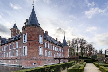 16. yüzyıl Alden Biesen kalesi, hendek ve Fransız bahçesi, dairesel kuleler, ahşap köprü ve arka planda çıplak ağaçlar, tuğla duvarlar, çatı, Bilzen, Limburg, Belçika 'da bulutlu bir gün.