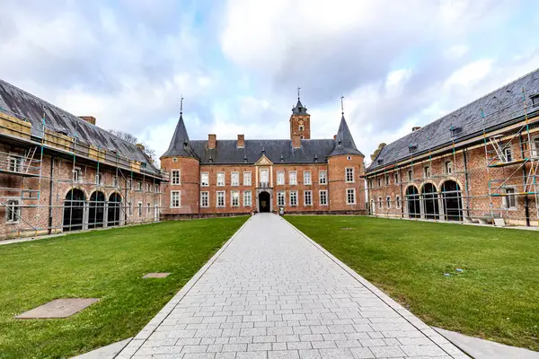 Straight path in outer courtyard in direction of Alden Biesen Castle between side buildings, rear facade, brick walls, gable roof and two towers, 16th century, cloudy day in Bilzen, Limburg, Belgium