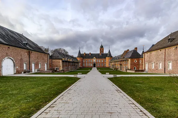 Rear exterior patio with straight cobbled path towards Alden Biesen Castle in background, brick walls and gable roof, 16th century, cloudy day with stormy cloudy sky in Bilzen, Limburg, Belgium