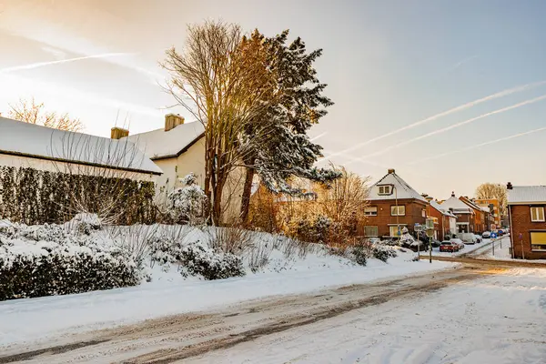 Winter urban street landscape, snow covered sidewalks and gardens, streets with salt to prevent cars from sliding or skidding, sunny sunrise after heavy snowfall in South Limburg, Netherlands