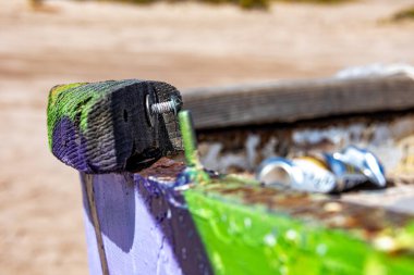 Eski bir teknenin pruvasının yakın çekimi, paslı vidalarla kahverengi arka plan, kabuğu soyulmuş yeşil ve mor renkli tekne gövdesi, Meksika sahillerinde güneşli bir gün.