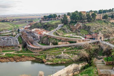 Kayalık tepeler, yeşil çimenler, binalar, kırsal taşıt yolları ve Tagus Nehri ile kaplı bir vadi. Güneşli İspanya 'da güneşli bir günde Alcazar' ın bir kısmı puslu ve bulanık arka planda görülüyor.