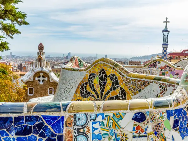 Parc Guell 'in Hypostyle' ının altındaki ana meydanda renkli mozaikler, arka planda bulutlu gökyüzüne karşı şehir manzarası, Barselona, Katalonya, İspanya 'da güneşli bir gün