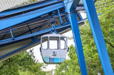 Dev bir metal yapıda teleferiğe asılı boş bir kulübe, Rheinpark 'taki istasyon, arka planda yeşil yaprak döken ağaçlar, Almanya' nın Köln şehrinde bulutlu bir bahar günü