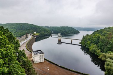 Gileppe Barajı 'nın havadan görünüşü, tepe üzerinde yaya yolu olan duvar, göl sularından çıkan iki giriş veya çıkış kulesi, vadi dağlarındaki yemyeşil ağaçlar, Jalhay, Belçika' da bulutlu bir gün.