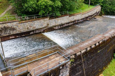 Robertville Barajı 'nda su Warche Nehri' ne akarken basamaklı destek sızıntısı. Arka planda yeşil ağaçlar. Waimes, Belçika 'da bulutlu bir gün.