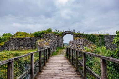 Logne Kalesi 'nin kemerli kapısına giden tahta köprü, gri bulutlarla kaplı gökyüzüne karşı eskimiş taş duvar, Belçika, Ferrieres' de bulutlu bir gün.