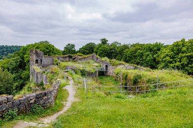 Logne Şatosu tepede yıkıldı, zamanın geçişi ile taş duvarlar yıkıldı, koruma için metal korkuluklar, arka planda yemyeşil ağaçlar, Ferrieres, Belçika 'da bulutlu bir gün