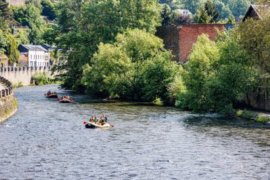 La Roche-en-Ardenne, Belçika. 4 Haziran 2024. River Ourthe turistlerle birlikte üç şişme kayıkta yelken açıyorlar, binalar, taş duvarlar ve yeşil ağaçlar güneşli bir yaz gününün keyfini çıkarıyorlar.