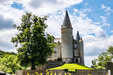 Veves Kalesi tepede mavi gökyüzüne karşı, konik çatıları ve taş duvarları olan kuleler, yeşil yapraklı dev bir ağaç, Houyet, Namur 'da güneşli bir gün, Wallonia, Belçika