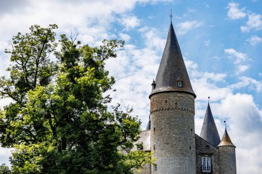 Konik çatıları ve Veves Kalesi 'nin taş duvarları olan kuleler, yeşil yapraklı dev ağaç, mavi gökyüzü ve beyaz bulutlarla güneşli bir gün Houyet, Namur vilayeti, Wallonia, Belçika