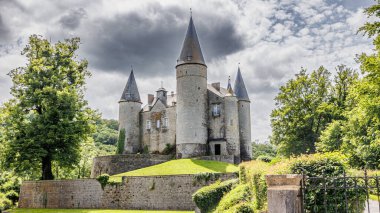 Veves Castle tepede, arka planda fırtınalı gri gökyüzü, yeşil yapraklı ağaçlarla çevrili, konik çatıları olan taş kuleleri olan, güneşli bir gün Houyet, Namur, Wallonia, Belçika