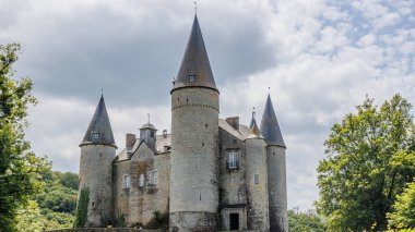 Yeşil yapraklı ağaçlarla çevrili taş kuleleri olan Veves Kalesi. Arka planda fırtınalı gri gökyüzü. Houyet, Namur, Wallonia, Belçika 'da güneşli bir gün.