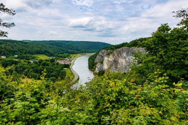 Meuse Nehri, Freyr Kalesi ve büyük Freyr Kayaları oluşumuyla vadiyi kaplayan yeşil yapraklı ağaçlar Namur, Wallonia, Belçika 'da bulutlu bir yaz günü