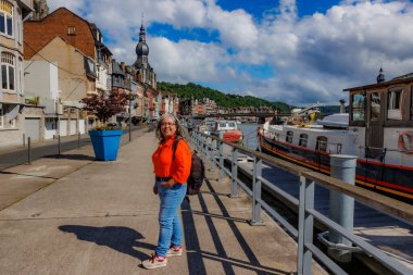 Meuse nehri, şehir manzarası ve arkadaki kolej kulesi boyunca gezinti yapan kıdemli yetişkin turist, güneşli bir günde Dinant, Namur, Wallonia, Belçika 'yı turluyor.