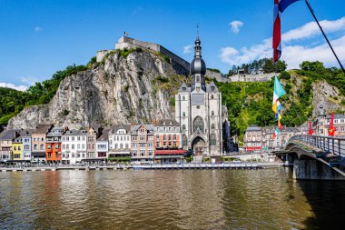 Kayalık dağın tepesinde kale ve Dinant Hanım 'ın kolej kilisesi, dalgalı bayraklı köprü, Meuse Nehri' ne bakan binalar, Namur, Wallonia, Belçika 'da güneşli bir yaz günü.