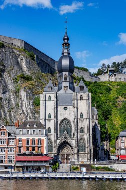 Dinant 'ın kolej kilisesi, arka planında kale olan dağ, tatil köyünde Meuse nehrine bakan binalar, güneşli bir yaz günü Namur, Wallonia, Belçika