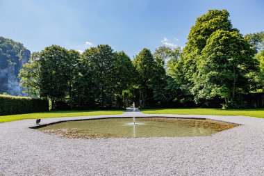 Freyr Kalesi 'nde granit taşlarla çevrili bir fıskiyeyle çevrili yeşil yapraklı ağaçlar arka planda mavi gökyüzüne karşı, güneşli bir yaz günü Namur, Wallonia, Belçika' da