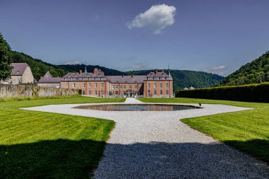 Freyr Kalesi 'nin girişi ve cephesi, arka planda çeşme ve Rönesans tarzı binalar, masmavi gökyüzüne karşı yemyeşil ağaçlı dağlar, Namur, Wallonia, Belçika' da güneşli bir yaz günü.