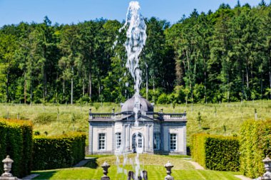 Arka planda Rönesans tarzı bina Freyr Kalesi 'ndeki çeşmeden fışkıran su jeti, mavi gökyüzüne karşı yemyeşil ağaçlar, Namur, Wallonia, Belçika' da güneşli bir yaz günü