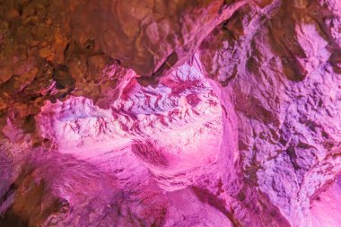 Neptün Mağaraları, Couvin, Wallonia, Belçika 'daki su sızıntısı nedeniyle yapay mor-pembe ışık, çatlak, pürüzlü ve düzensiz duvarlarla aydınlatılmış bir yeraltı kaya oluşumundaki tünel.